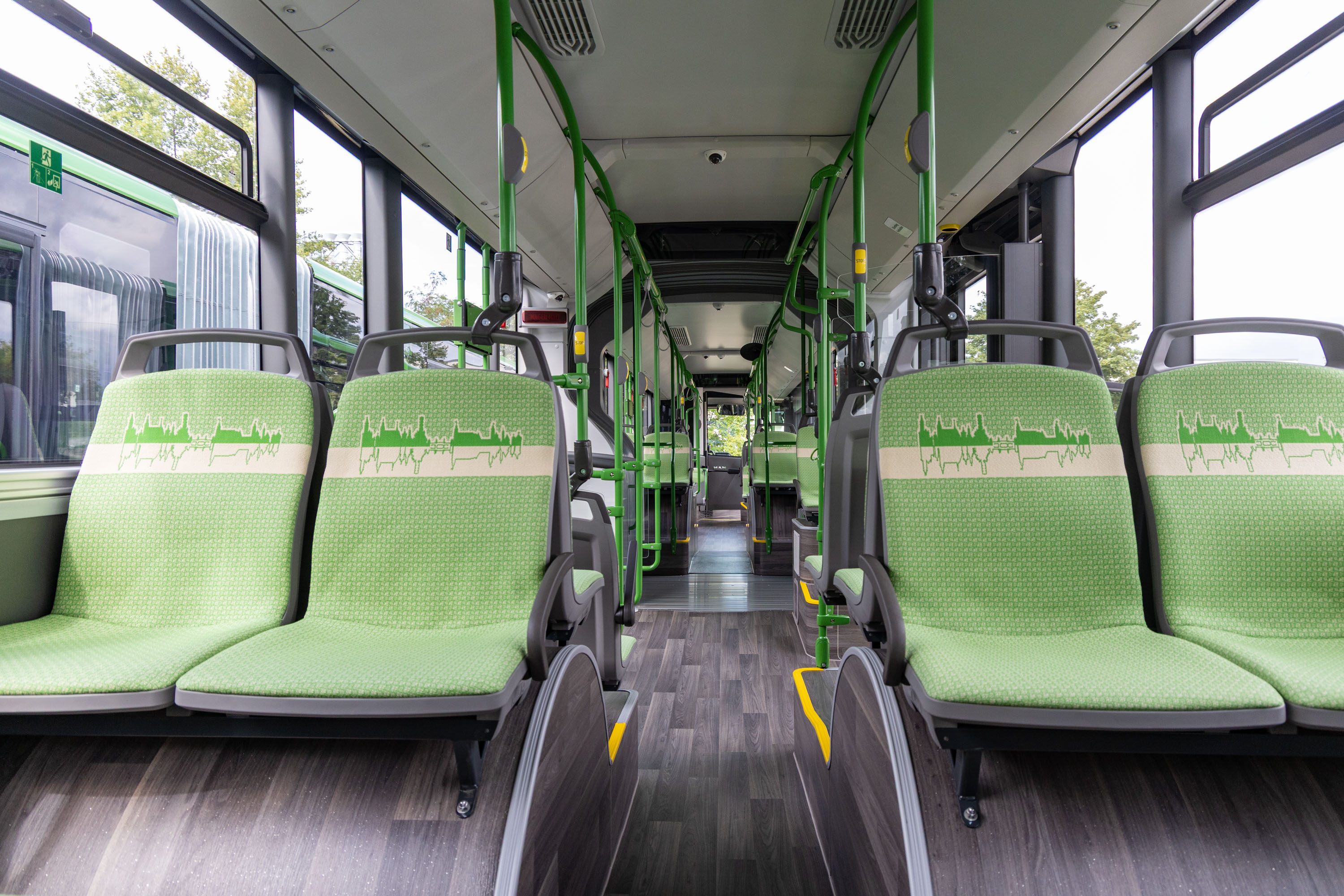 Bild zeigt den modernen Innenraum der neuen Busse mit Böden in dunkler Holzoptik und den hellgrünen Sitzen, welche auch aus den neuen SKODA Straßenbahnen bekannt sind.